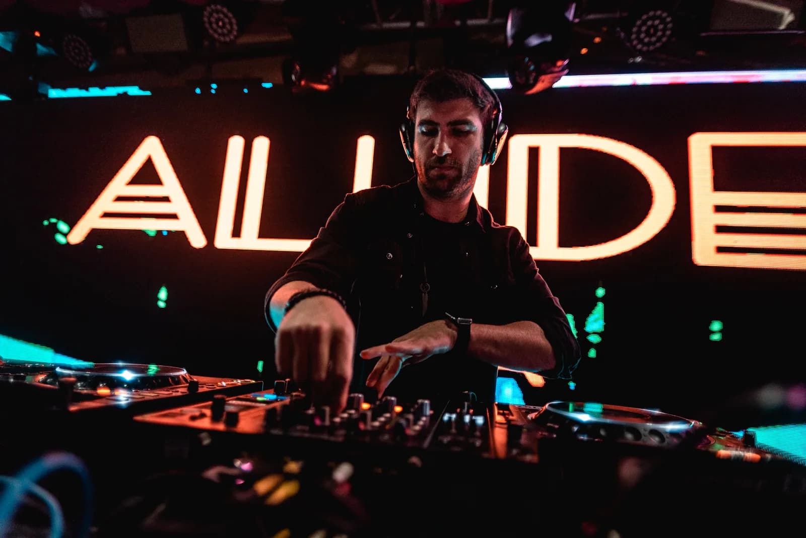 Alude tocando com o letreiro ALUDE em neon aceso atrás